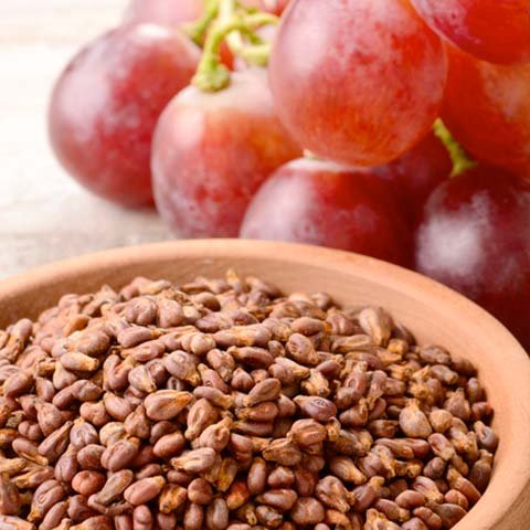 Grape seeds in wooden bowl with red grapes - powerful antioxidant source for vascular health and performance